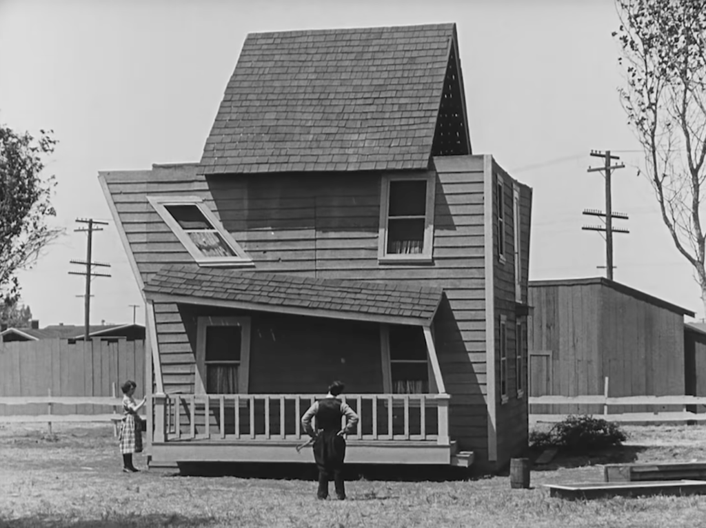 Still from the Buster Keaton short "One Week" in which Keaton examines a misshapen, poorly built house.
